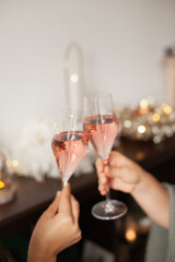 Wall Mural - Holding two glasses of rose sparkling wine to cheers for Christmas or New year. Celebrating at party. Happy Birthday or anniversary. Festive drinks background