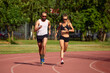© Georgii - Young family promoting healthy lifestyle. Woman and man run stadium. Coach and sportsman motion run training before race. Couple runners training outdoors. Couple or family live healthy lifestyle.