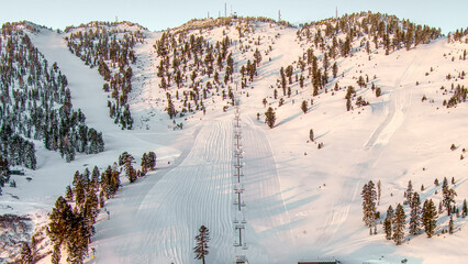 Wall Mural - Fresh groomed ski run with a ski chairlift on a steep snowcapped mountain
