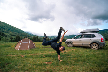 Concept of success and achievement. The man have fun (dances) on the top of mountains. A tourist tent and a four-wheel drive car with a roof rack. Travel and vacation