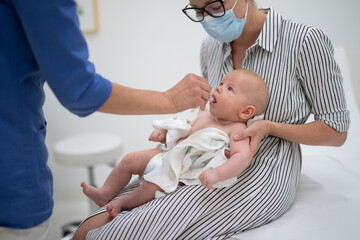 Wall Mural - Pediatrician administring oral vaccination against rotavirus infection to little baby in presence of his mother. Children health care and disease prevention.