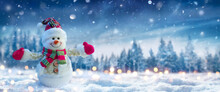 Snowman On Snow In Winter Forest With Snowfall In Defocused Landscape And Abstract Lights
