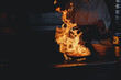 © Parilov - Process professional chef and fire pan. Woman cooking food vegetable open fire, dark background