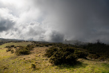 Dramatic Landscape Of Storm Clouds, Fog, And Grassy Meadow And Hills