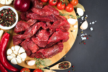 Wall Mural - Veal meat for cooking stew, azu or other meat main dish. Chopped raw beef or lamb meat with seasonings, herbs and vegetables on wooden plate over black background. View above