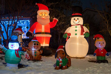 Inflatable Figures Of Santa Claus, Elf And Snowman Glowing At Night. Christmas And New Year Holiday Decorations. Selective Focus, Blurred Background