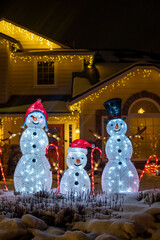 Wall Mural - Glowing snowmen figures at night. Beautiful Christmas illuminated decorations outside the house. Selective focus, blurred background