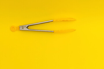 Wall Mural - Yellow pasta tongs on yellow background, monochrome