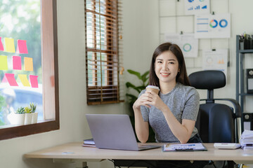 Asian businesswoman working on financial paperwork using laptop online tax, loan, bank debt for mathematical finance on desk, accounting, statistics and analytical research concept.