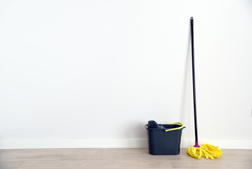 Una fregona y un cubo gris delante de una pared blanca en una habitación vacía.