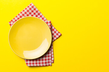 Wall Mural - Top view on colored background empty round yellow plate on tablecloth for food. Empty dish on napkin with space for your design