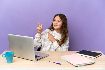 Canvas Print - Little student girl in a workplace with a laptop isolated on purple background pointing with the index finger a great idea