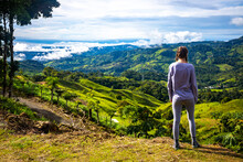 Girl Stands On Hill Admiring Idyllic Landscape Of Costa Rican Mountains; Green Slopes Bathed In Clouds In Costa Rica