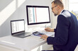 © Studio Romantic - Concentrated male financial director in office works using electronic invoice software. Man with calculator and two computers and works with spreadsheets to calculate report on financial data.