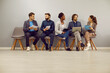 © Studio Romantic - Diverse job seekers talking to each other while waiting for job interview. Multiracial group of people sitting in row by office wall, waiting for business meeting and discussing different work topics