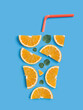 Refreshing summer cocktail concept. Creative flat lay arrangement of orange slices, fresh mint leaves and drinking straw in the shape of a glass with refreshing orange juice on light blue background