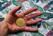 Close-up Of A Bitcoin In The Palm Of A Man's Hand, With A Tropical Phono.