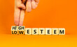 High or low esteem symbol. Concept words High esteem and Low esteem on wooden cubes. Businessman hand. Beautiful orange table orange background. Business high or low esteem concept. Copy space.