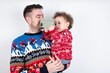 © Jihan - Man holding his beautiful little son with curly hair wearing red Christmas knitted sweater against white background holding smartphone making video call greeting holidays or watching Christmas videos