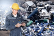 © scharfsinn86 - A worker with a digital tablet at a waste recycling plant. Waste management concept