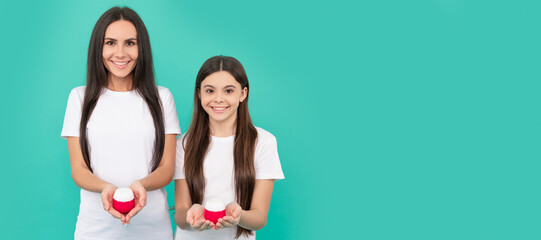 Canvas Print - Mother and daughter child banner, copy space, isolated background. positive mother and daughter hold cream jar on blue background.