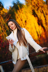 Wall Mural - Female model with mobile outdoor. Young pretty woman with phone on autumn park background.