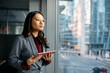 © Drazen - Pensive Asian businesswoman with touchpad looking through window in office.