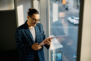 Wall Mural - Happy Hispanic businesswoman working on digital tablet by window in office.