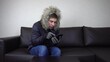 © Vital9c - A young man is sitting at home in a winter jacket and trying to keep warm. A man sits without heating and calls on the phone and asks for help.