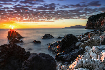 Wall Mural - colorful sunrise at Cala Gonone with black and white rocks and boulders in the foreground