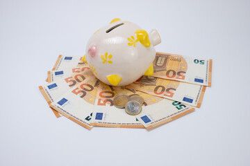 Piggy bank on top of fifty euro banknotes with one and tow euros coins, on a white background. Top view. Concept of saving money. copy space.