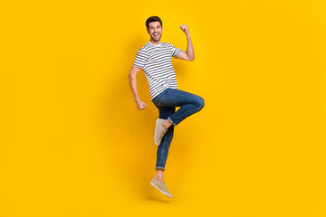 Canvas Print - Full length photo of cool lucky guy dressed striped t-shirt rising fist jumping high isolated yellow color background