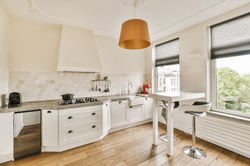 Wall Mural - a kitchen with wood flooring and white cabinets in the center of the image is an orange pendant light hanging over the sink