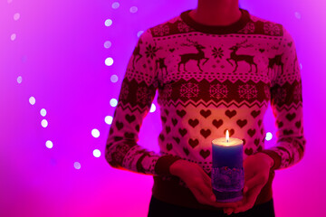 Woman holding christmas candle with christmas trees. She is wearing a Christmas sweater with reindeers. Picture in pink and purple tones - refers to Christmas.     