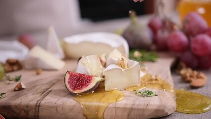 Wall Mural - Woman pours walnuts on a Sliced pieces of Camembert or brie cheese on wooden cutting board at domestic kitchen