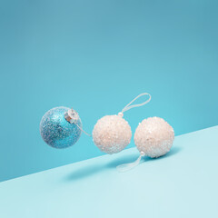 Wall Mural - Christmas and New Year scene with three snowy bauble on a pastel blue background. Tilted angle view. Trendy winter holidays composition.