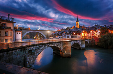 Stunning vivid cityscape. Scenic view Historical Old Town of Bern city with colorful sky, view on bridges over Aare river and church tower during dramatic sunset. Bern. Switzerland. Europe