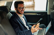 © Kostiantyn - Attractive businessman in suit use phone and working laptop while riding in car to office