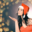 © yurolaitsalbert - woman in costume of Santa Claus showing to copy space. Beautiful bokeh effect from a garland.