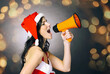 © yurolaitsalbert - young woman dressed as Santa Claus shouting into a megaphone. Beautiful bokeh effect from a garland.