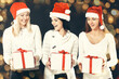© yurolaitsalbert - three young women in costume of Santa Claus with Christmas shopping. Beautiful bokeh effect from a garland.