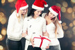 © yurolaitsalbert - three women in costume of Santa Claus with Christmas shopping. Beautiful bokeh effect from a garland.