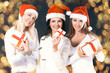 © yurolaitsalbert - three women in costume of Santa Claus with Christmas shopping. Beautiful bokeh effect from a garland.