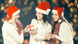 © yurolaitsalbert - three happythree happy young girls dressed as Santa Claus sitting with a bunch of Christmas gifts. Beautiful bokeh effect from a garland.