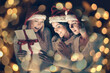 © yurolaitsalbert - group of female students in costumes of Santa Claus opening a box of Christmas gifts. Beautiful bokeh effect from a garland.