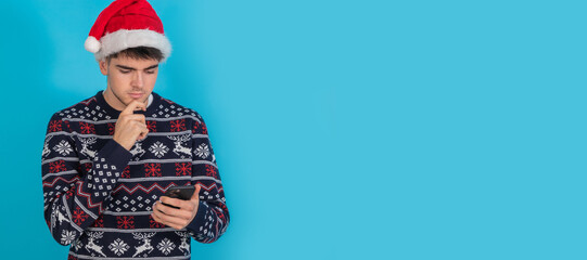 Poster - isolated young man in christmas clothes and santa claus hat with mobile phone or smartphone