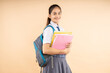 Happy Indian student modern schoolgirl wearing uniform holding books and bag standing isolated over beige background, Education  knowledge concept.  Copy space, Studio shot. 