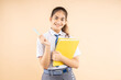Happy Indian student schoolgirl wearing school uniform holding books and bag standing isolated over beige background, Studio shot,closeup, Education concept.