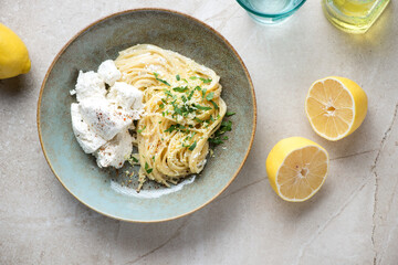 Wall Mural - Rustic plate with lemon and ricotta spaghetti on a beige stone background, horizontal shot, top view