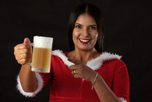 Beautiful Young Woman In Santa Claus Dress, On A Black Background, Holding A Glass Of Cold Beer